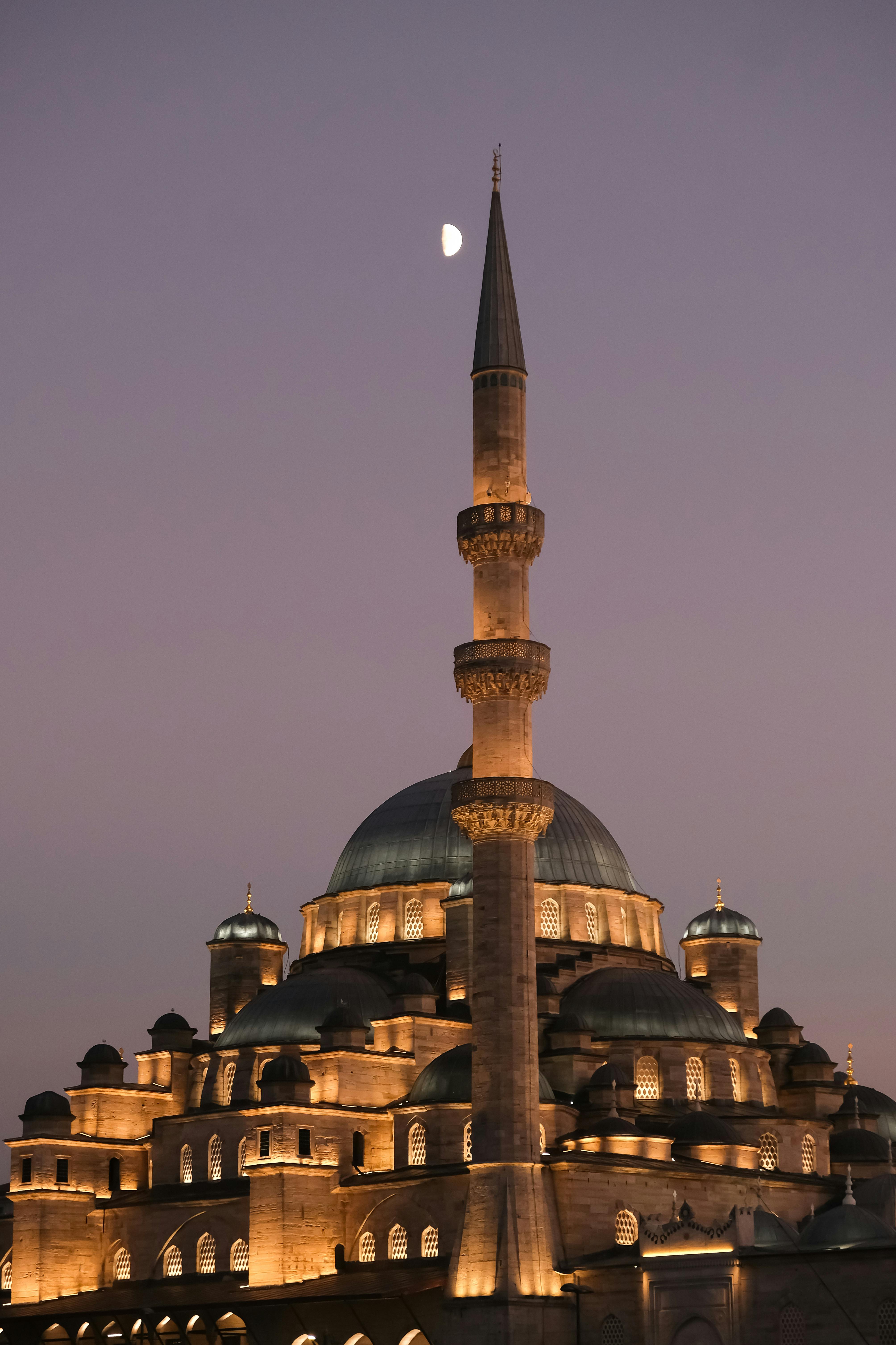 An iconic mosque in Istanbul illuminated at dusk with a crescent moon in the sky.