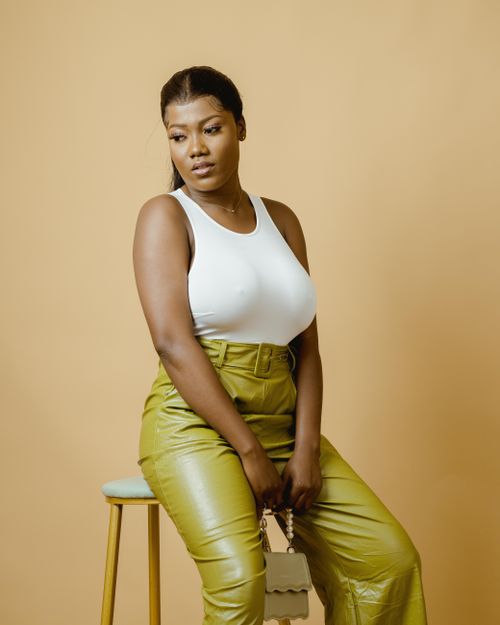 Free Fashionable portrait of a woman in leather pants and tank top against a yellow backdrop. Studio photography. Stock Photo