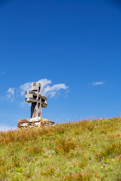 Free A wooden cross atop a grassy hill under a bright blue sky depicts serene natural beauty. Stock Photo