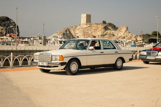 Classic Mercedes car parked by the seaside in İstanbul with a historic fort in the background.