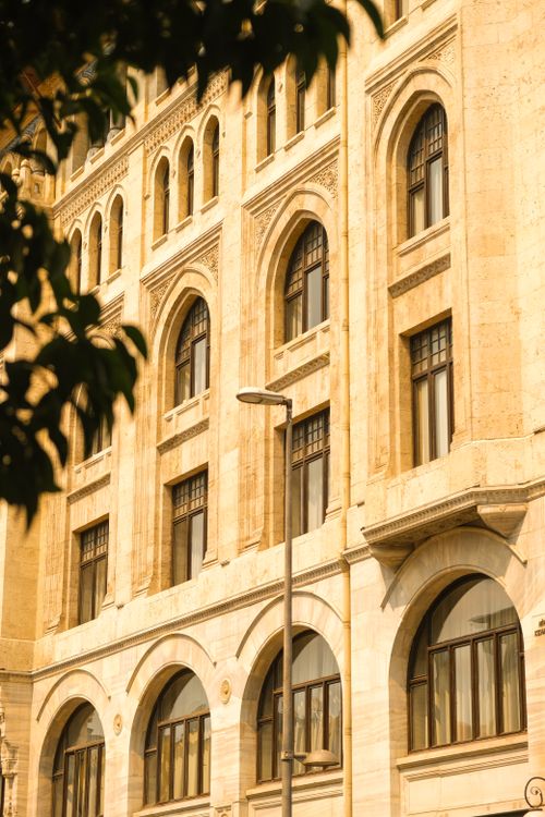 Free Detailed view of an ornate building facade showcasing arched windows under warm daylight, framed by foliage. Stock Photo