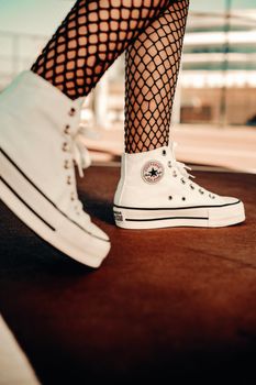 Stylish close-up of white sneakers and fishnet tights in an outdoor setting.