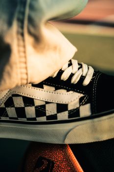 Artistic close-up of a checkered sneaker with cream pants on a basketball, captured in warm lighting.