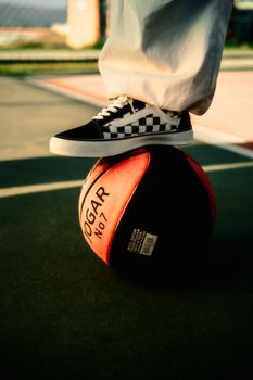 Close-up of a person wearing checkered sneakers while standing on a basketball outdoors.