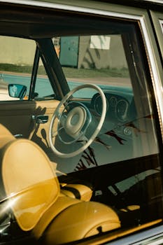 Close-up of a vintage car interior showcasing the steering wheel and seats under natural sunlight.