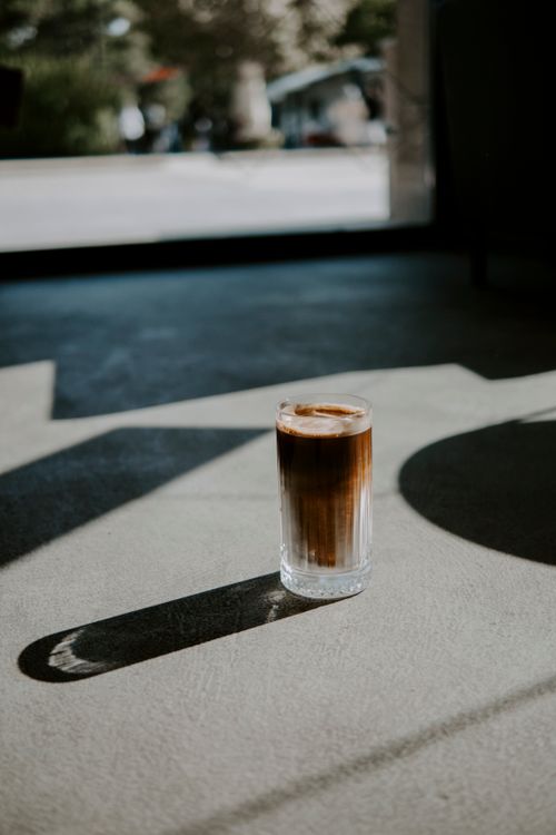 Free A sunlit glass of iced coffee casting shadows on a concrete floor indoors. Stock Photo
