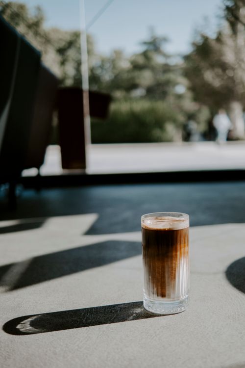 Free A refreshing iced coffee sits in a glass on a sunlit urban pavement. Stock Photo