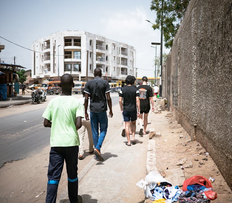 A group of people walking down a sunny street in Pikine, Dakar, Senegal, showcasing urban life.