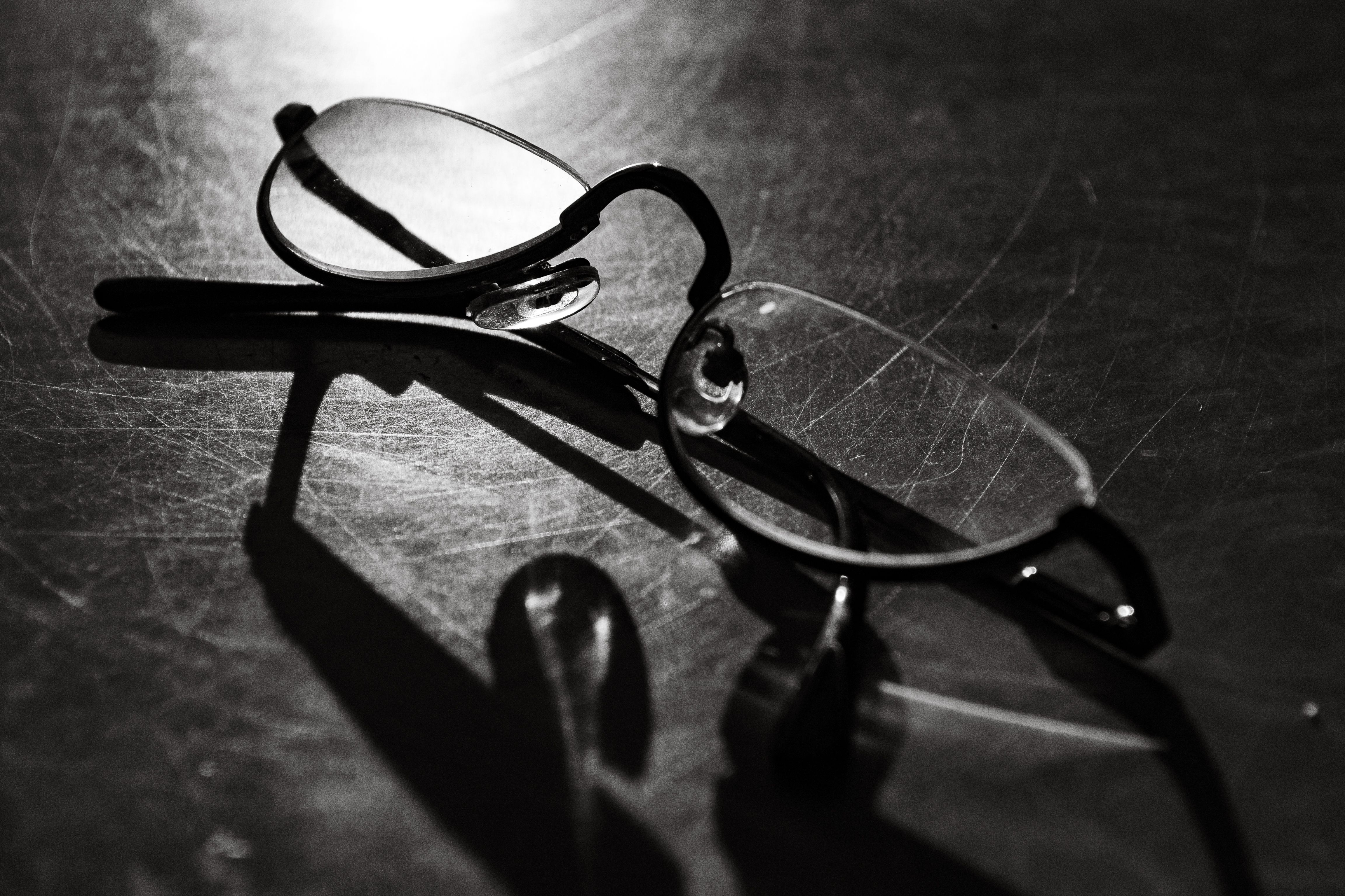 Black and white photo of eyeglasses with shadow on a reflective surface.