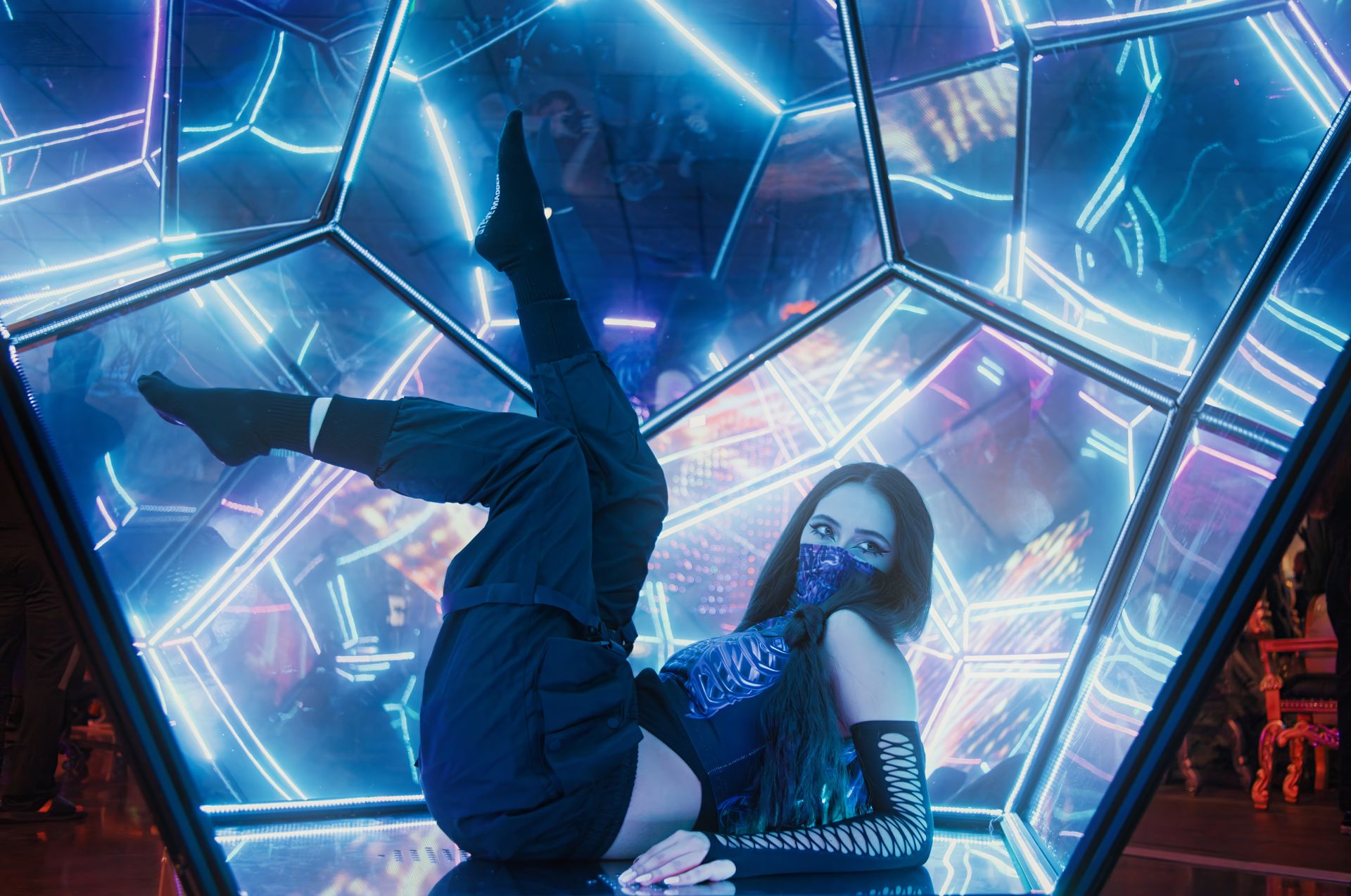 Woman in futuristic outfit poses amidst neon lights, combining artistry and technology.