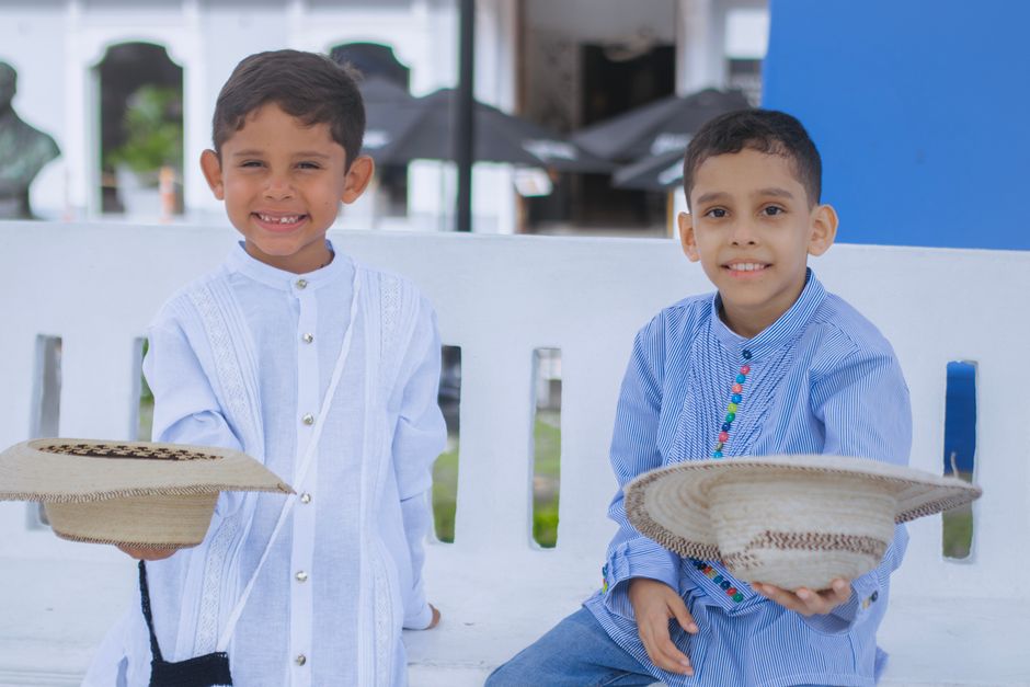 Fotomural Dos niños pequeños sonriendo y sosteniendo sombreros tradicionales de paja al aire libre en un banco.