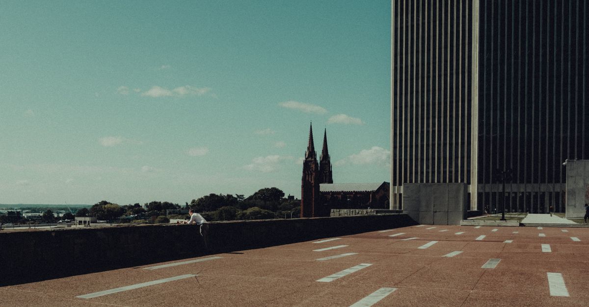 Wide view of a modern urban plaza with a cathedral spire in the background.