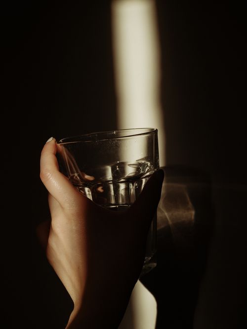Free Close-up of a hand holding a glass in dramatic lighting, creating striking reflections. Stock Photo