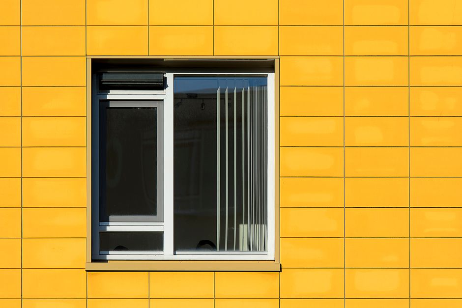 Close-up of a modern yellow building facade with a window, showcasing geometric architecture.