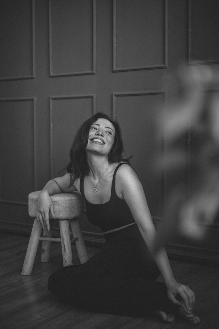 Smiling Woman Sitting On Floor And Leaning Arm On Stool