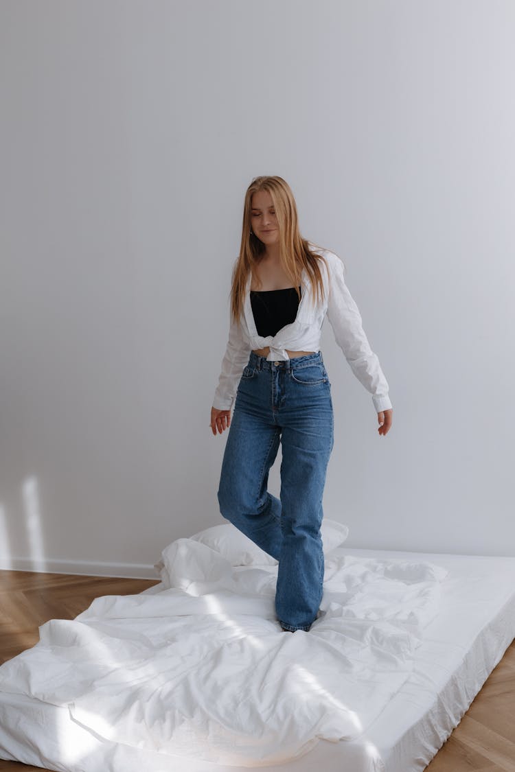 Young Woman Walking On Mattress With Sheets In Studio