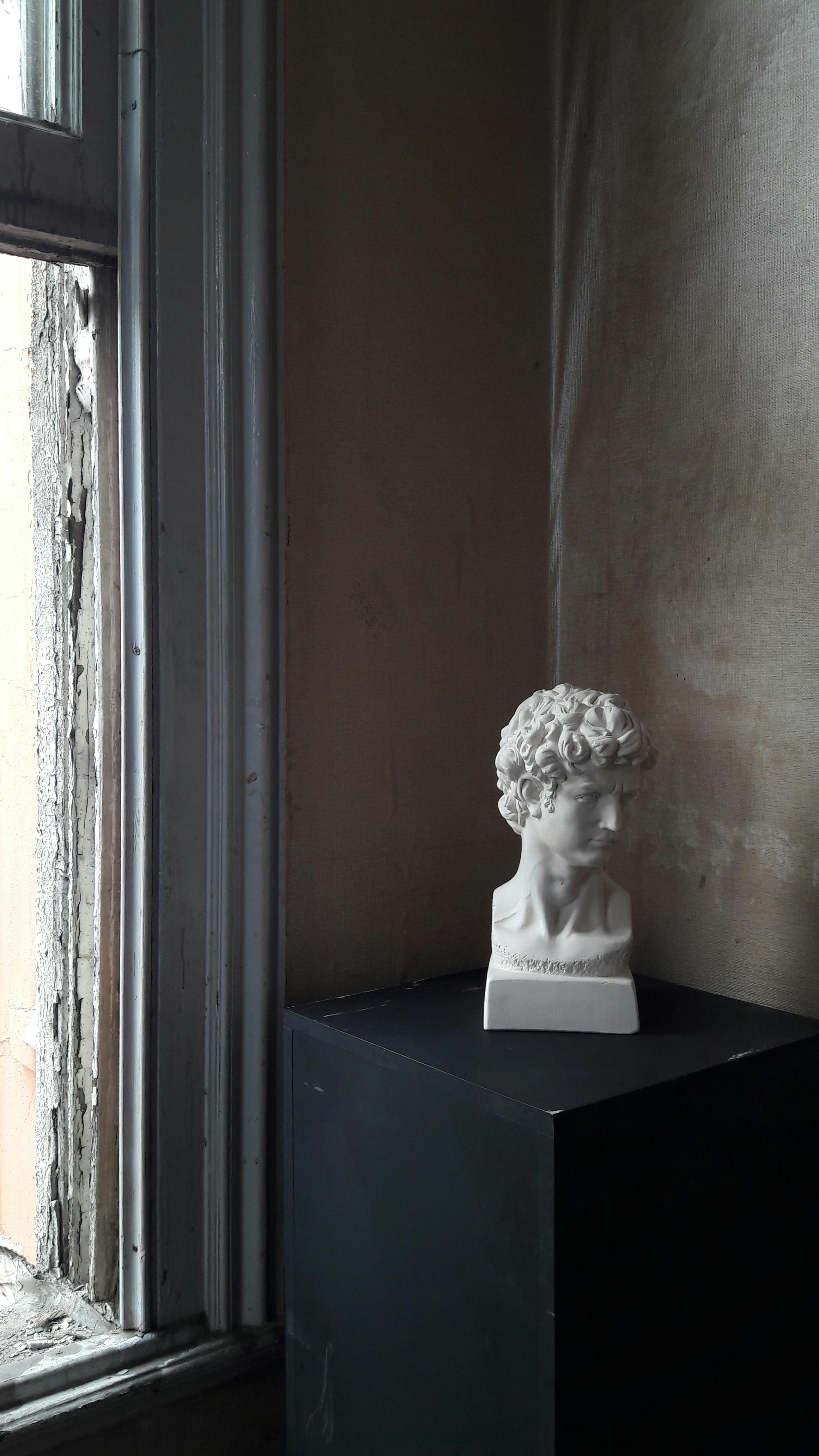 Free A marble bust displayed in a shadowy corner of a room, highlighting classical art. Stock Photo