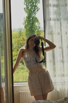 A woman taking a mirror selfie in a bright room with floral attire and casual style.