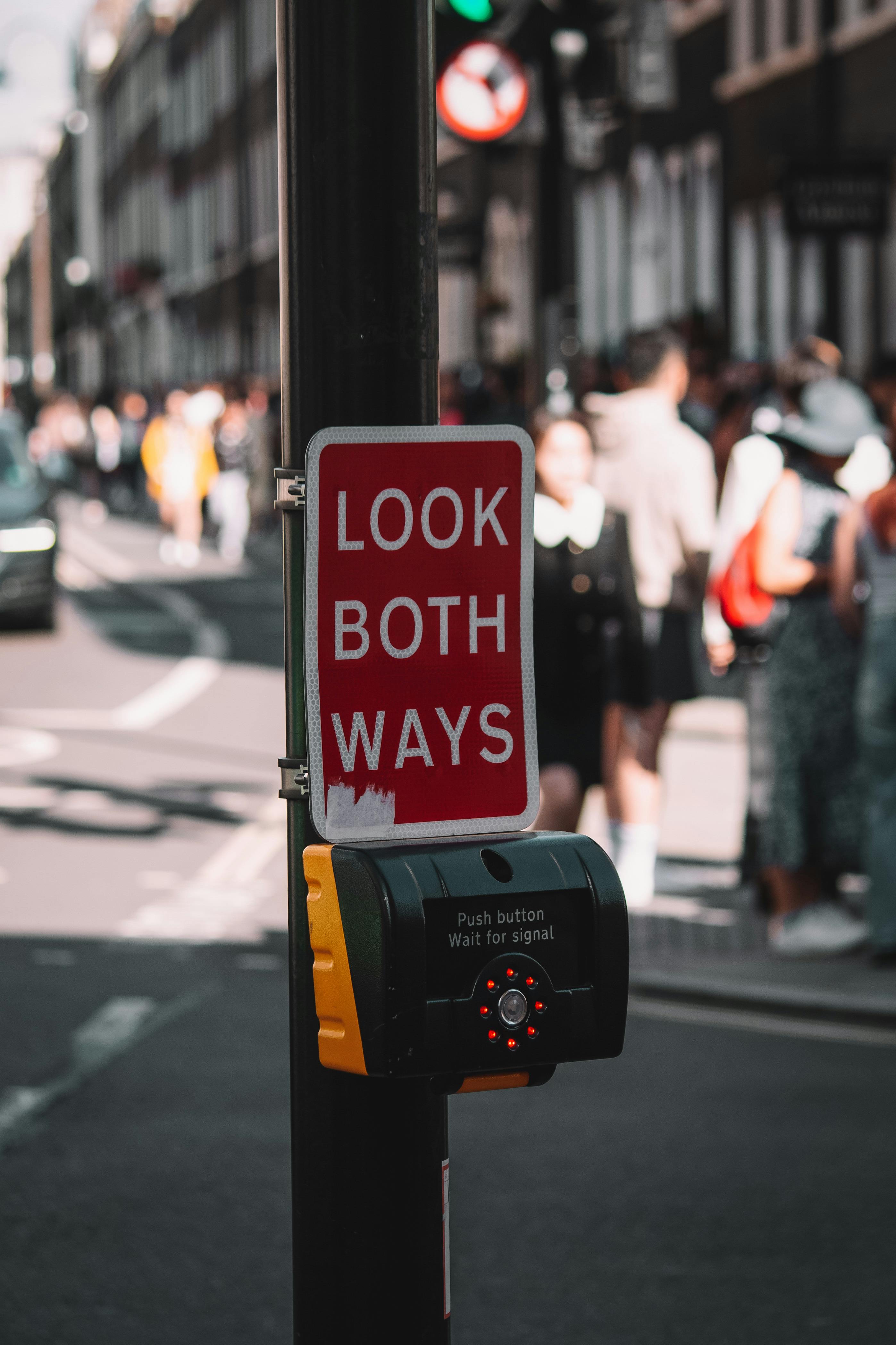 A busy London street crosswalk with a prominent 'Look Both Ways' sign and traffic light.