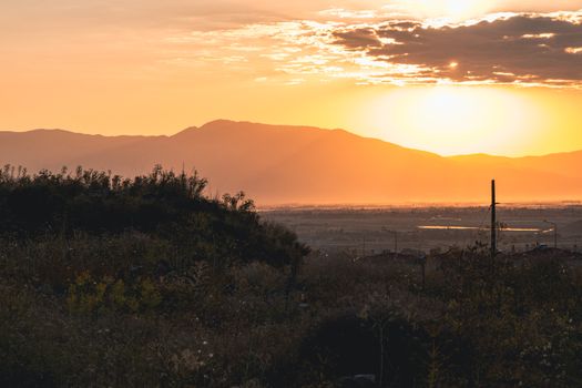 Capturing the tranquil beauty of a sunset over mountains with lush foliage and orange hues.