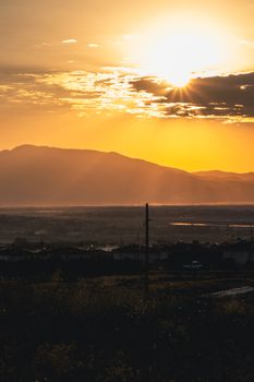 A picturesque golden hour sunset with dramatic clouds over rural mountains and countryside scenery.