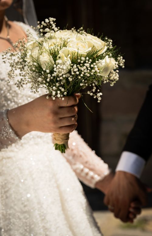 Free Close-up of a bride holding a bouquet while holding hands with the groom. Perfect for wedding themes. Stock Photo