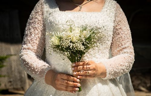 Free Bride in an embellished wedding dress holding a delicate white bouquet outdoors. Stock Photo