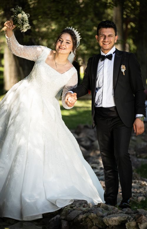 Free A smiling bride and groom stand hand in hand on rocks, showcasing wedding bliss. Stock Photo