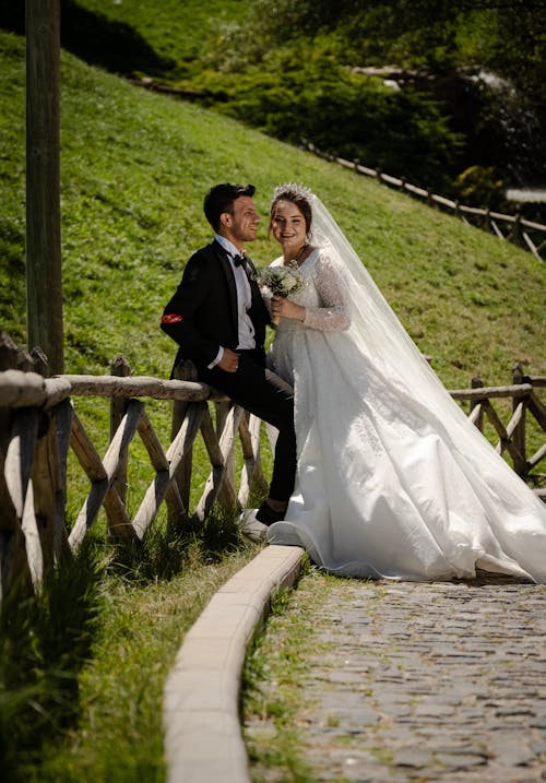 Smiling Newlyweds Posing by Wooden Fence in Village