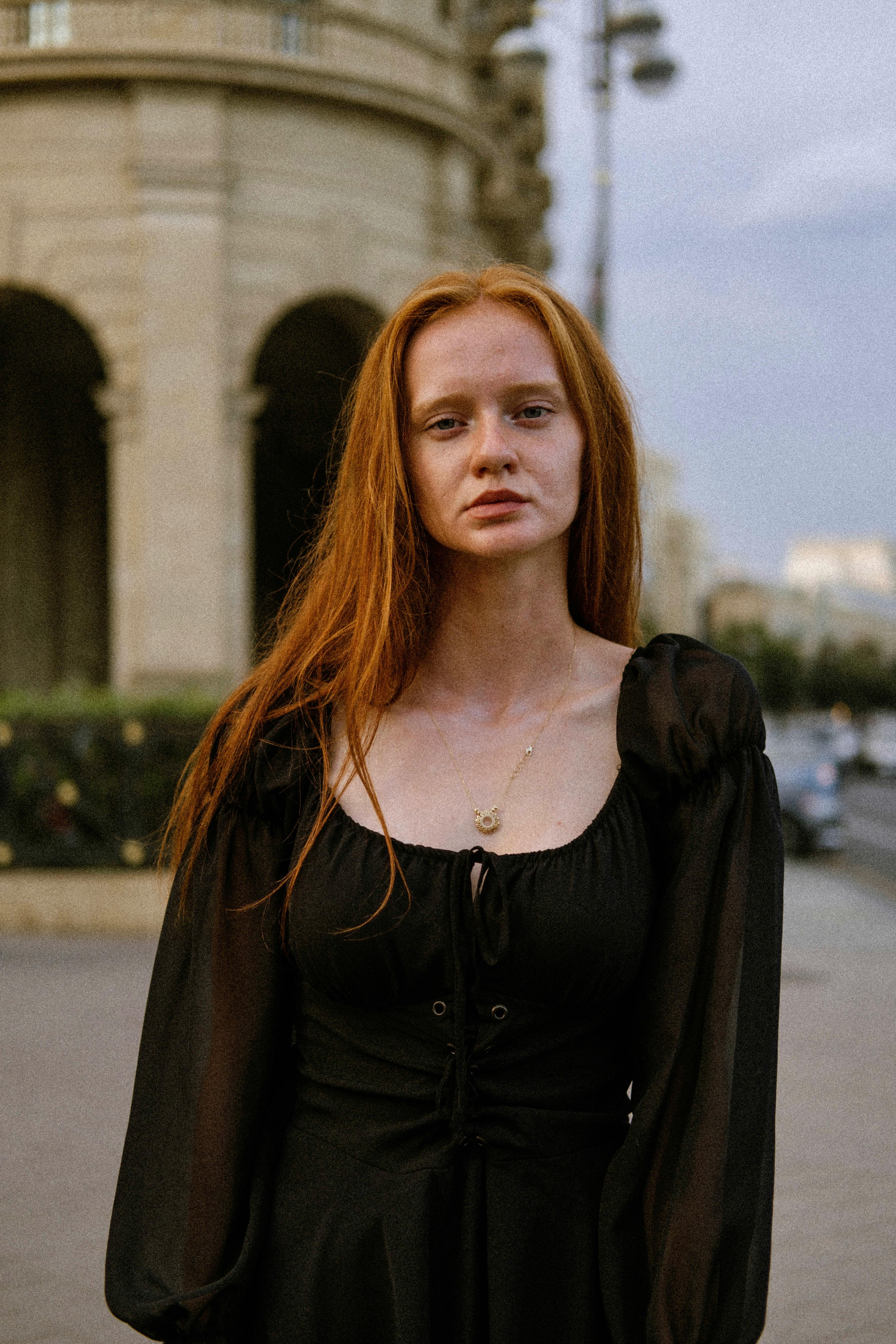Portrait of a young woman in a black dress standing in an urban environment.