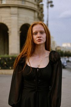 Portrait of a young woman in a black dress standing in an urban environment.
