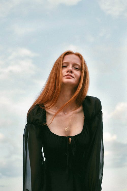 Free Bending Redhead Woman in Black Dress against Cloudy Sky Stock Photo