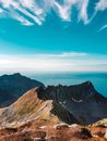 雄伟的山峰下，明亮的蓝天映衬着遥远的海景
