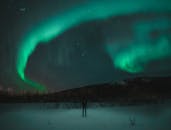 迷人的北极光照亮了白雪皑皑的景色，一个人正欣赏着繁星满天的夜空