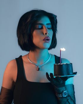 Stylish woman with short hair blowing out a candle on a black cake, showcasing elegance and celebration.