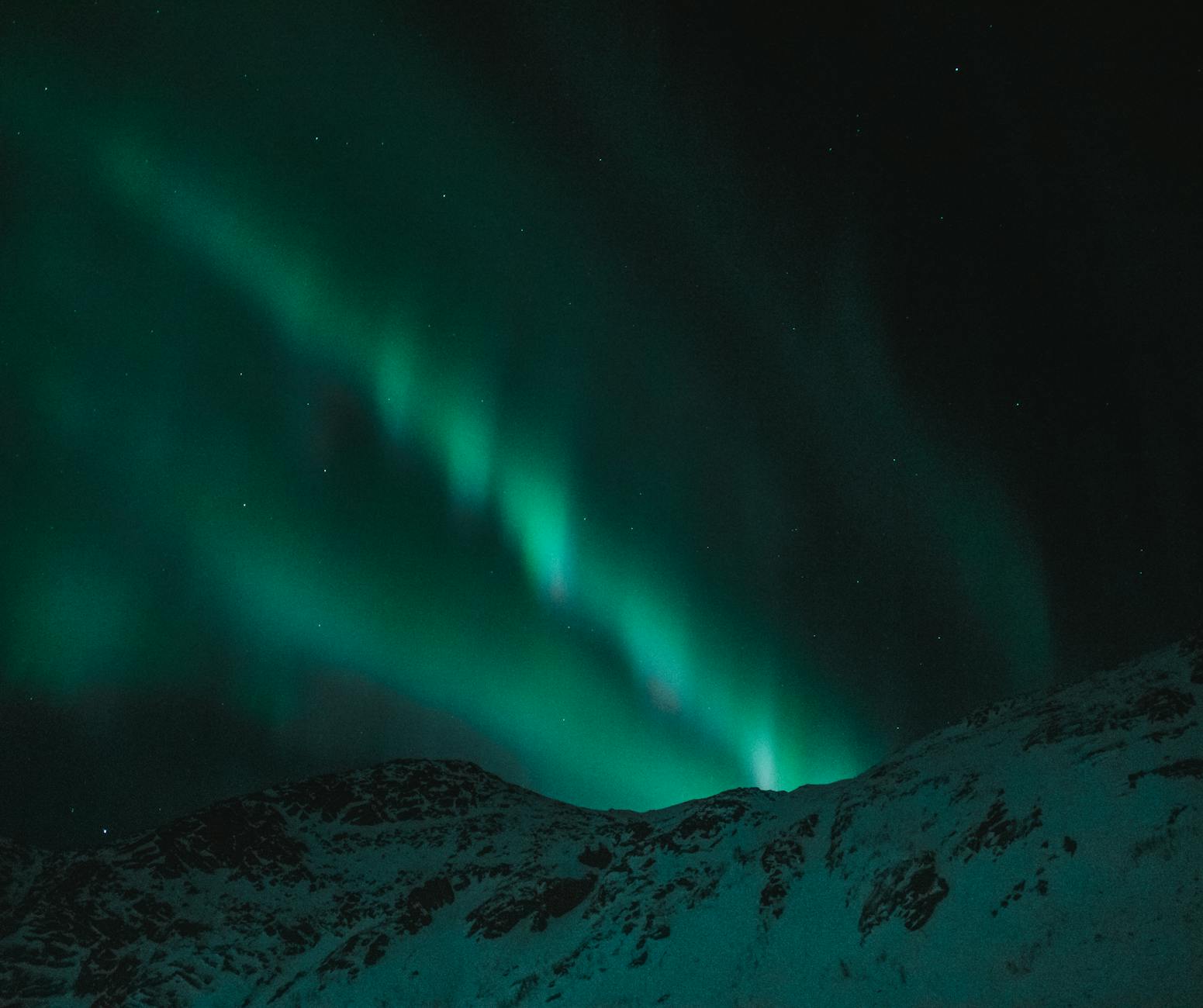 Northern lights over a snowy mountain top.