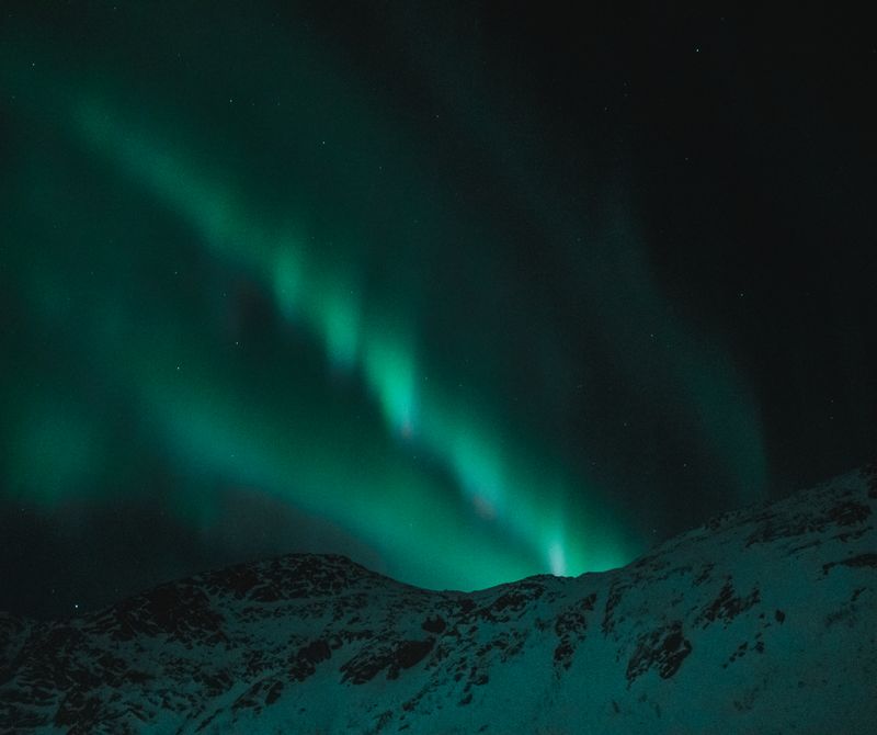 Aurora boreală verde deasupra munților acoperiți cu zăpadă, fotografie nocturnă
