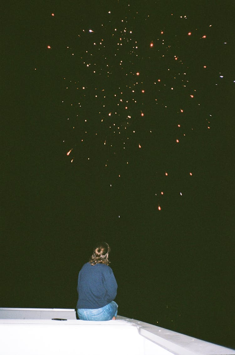 Woman Sitting At Night With Fireworks On Sky