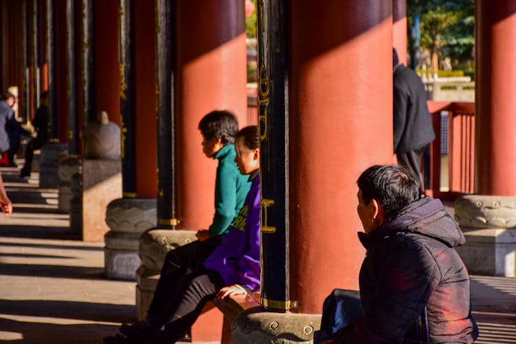 People Sitting On Benches Between Columns