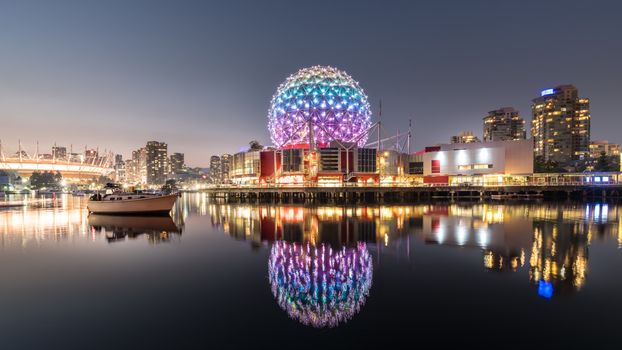 Colorful night view of Vancouver's Science World reflected in calm water, highlighting urban cityscape.