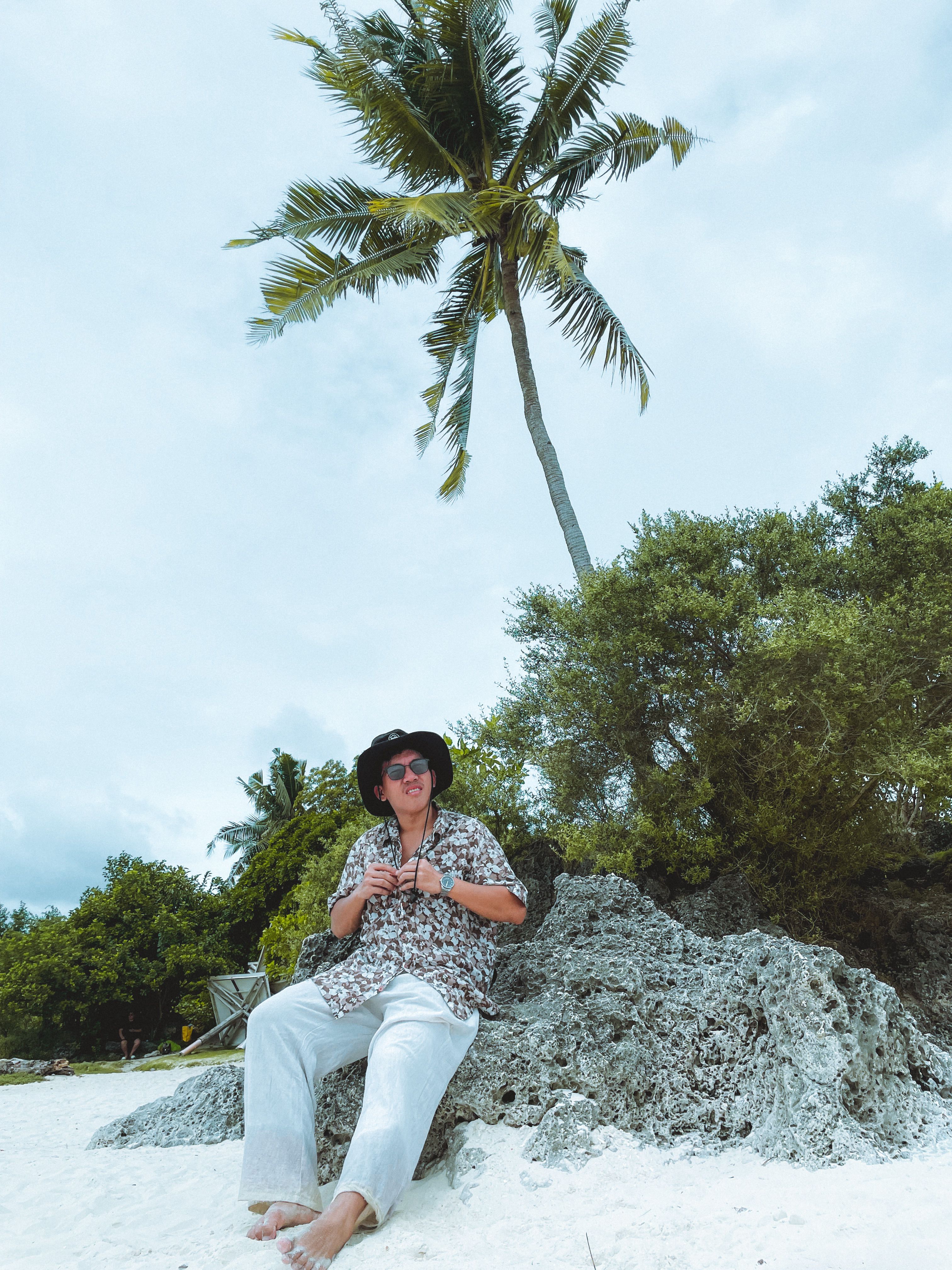 Man in Hawaiian Shirt Sitting on Rock at Tropical Beach · Free Stock Photo