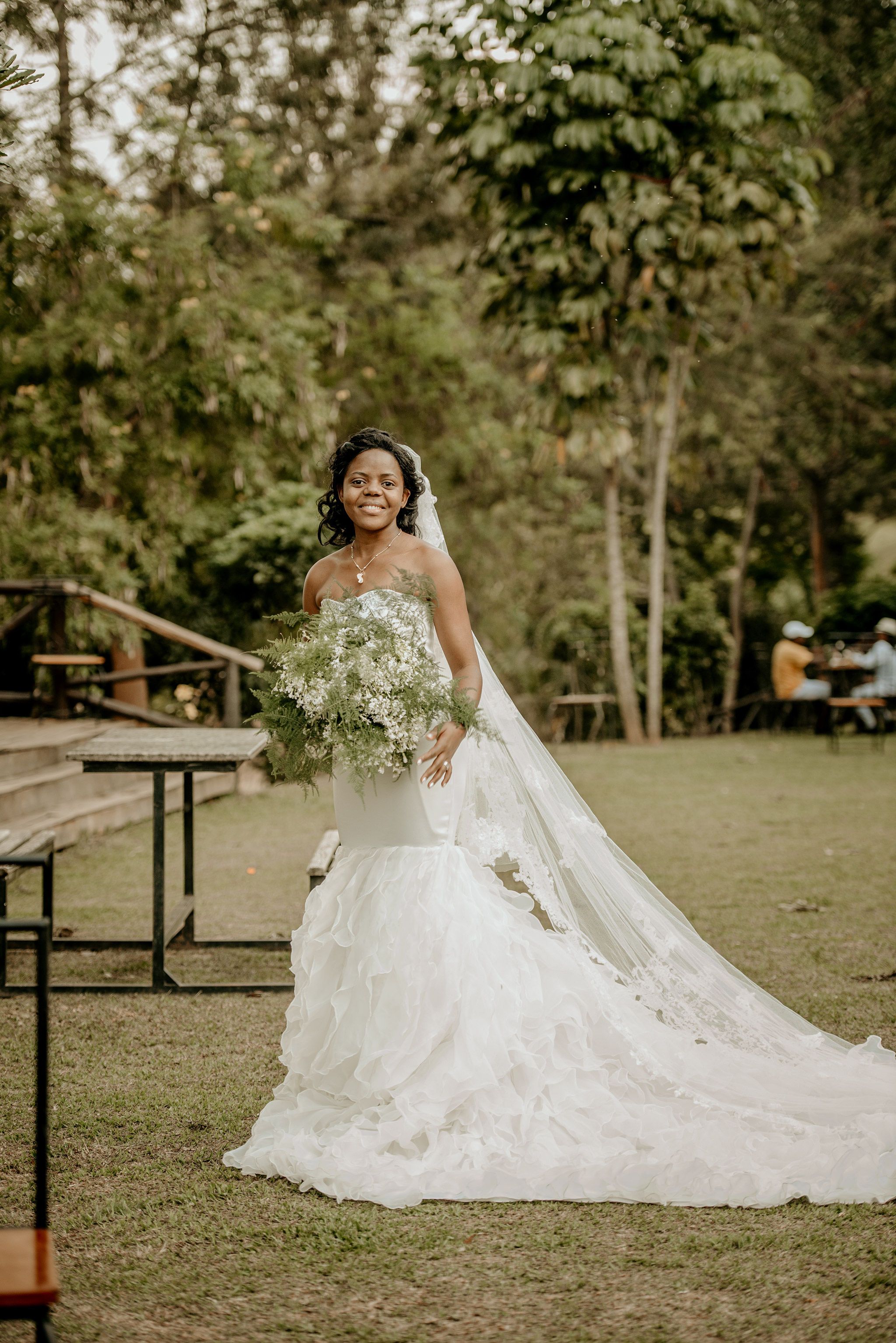 A joyful bride in a wedding dress posing outdoors with flowers in Kigali, Rwanda.