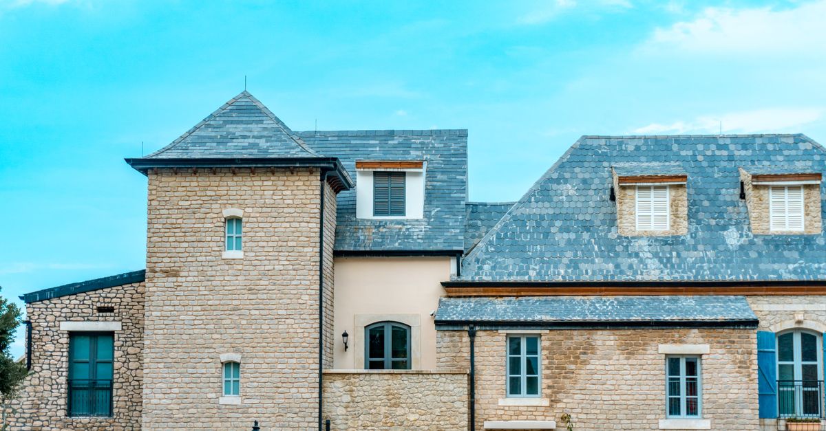 A picturesque stone house featuring a slate roof and blue shutters against a vibrant sky.