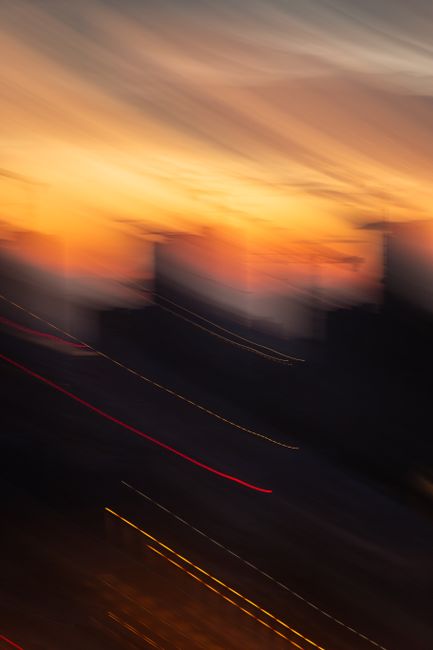 Vibrant sunset over blurred cityscape with artistic light trails.