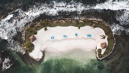 Free Drone shot of a tropical islet with palm trees, sunshades, and ocean waves. Stock Photo