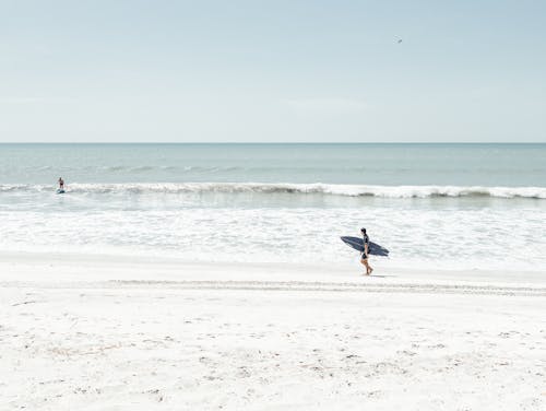Man Walking on Beach with Surfboard under Arm