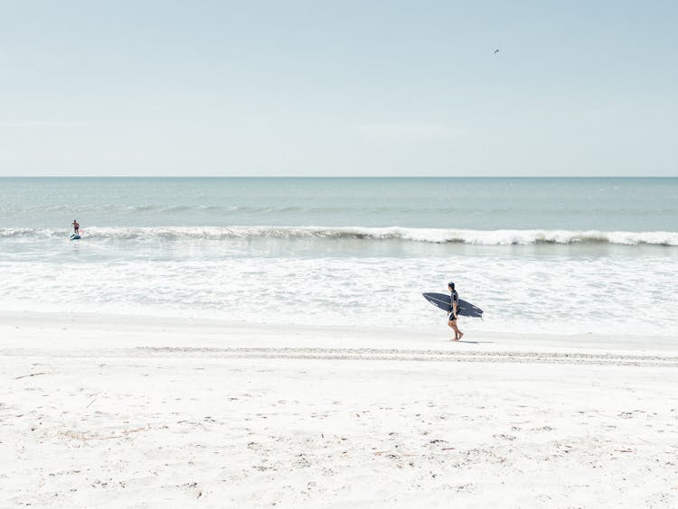 Man Walking On Beach With Surfboard Under Arm