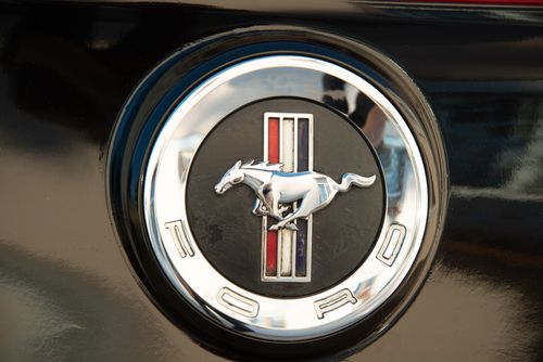 Free Detailed close-up of Ford Mustang emblem on a vehicle's black surface, symbolizing speed. Stock Photo