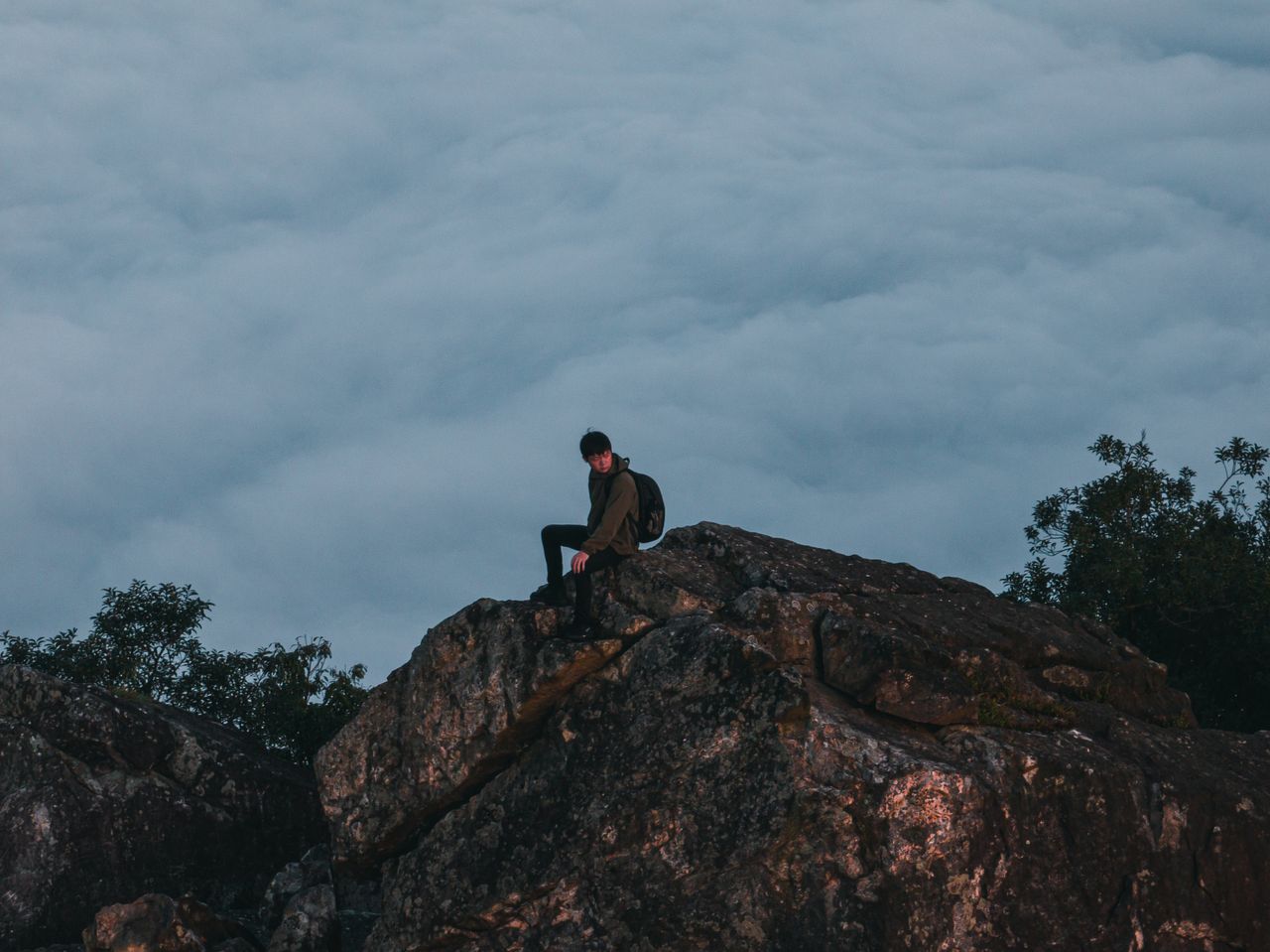 a lone backpacker sits on a mountain rock above clouds capturing a ser