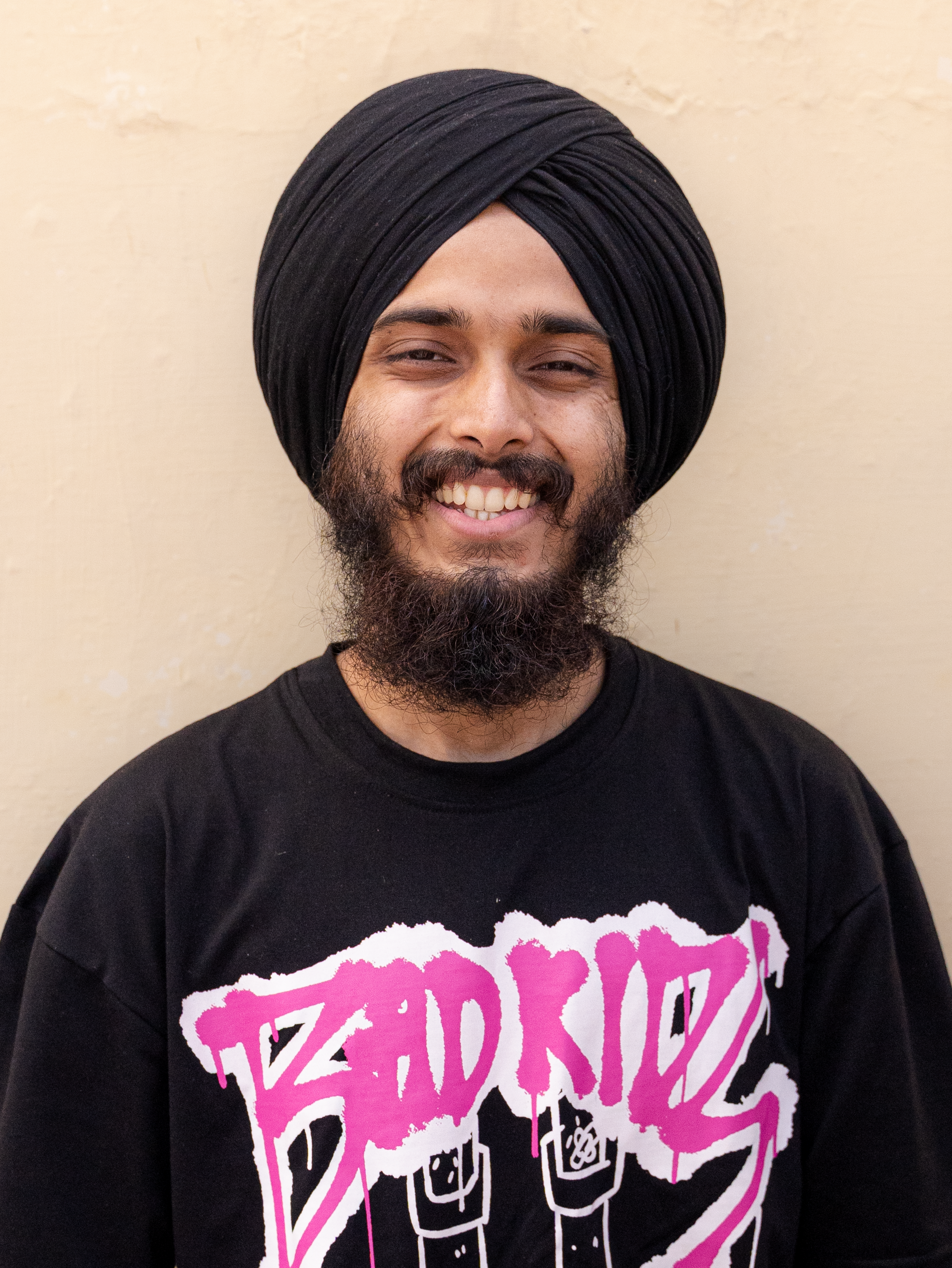 Portrait of a smiling man with a beard wearing a black turban and t-shirt.